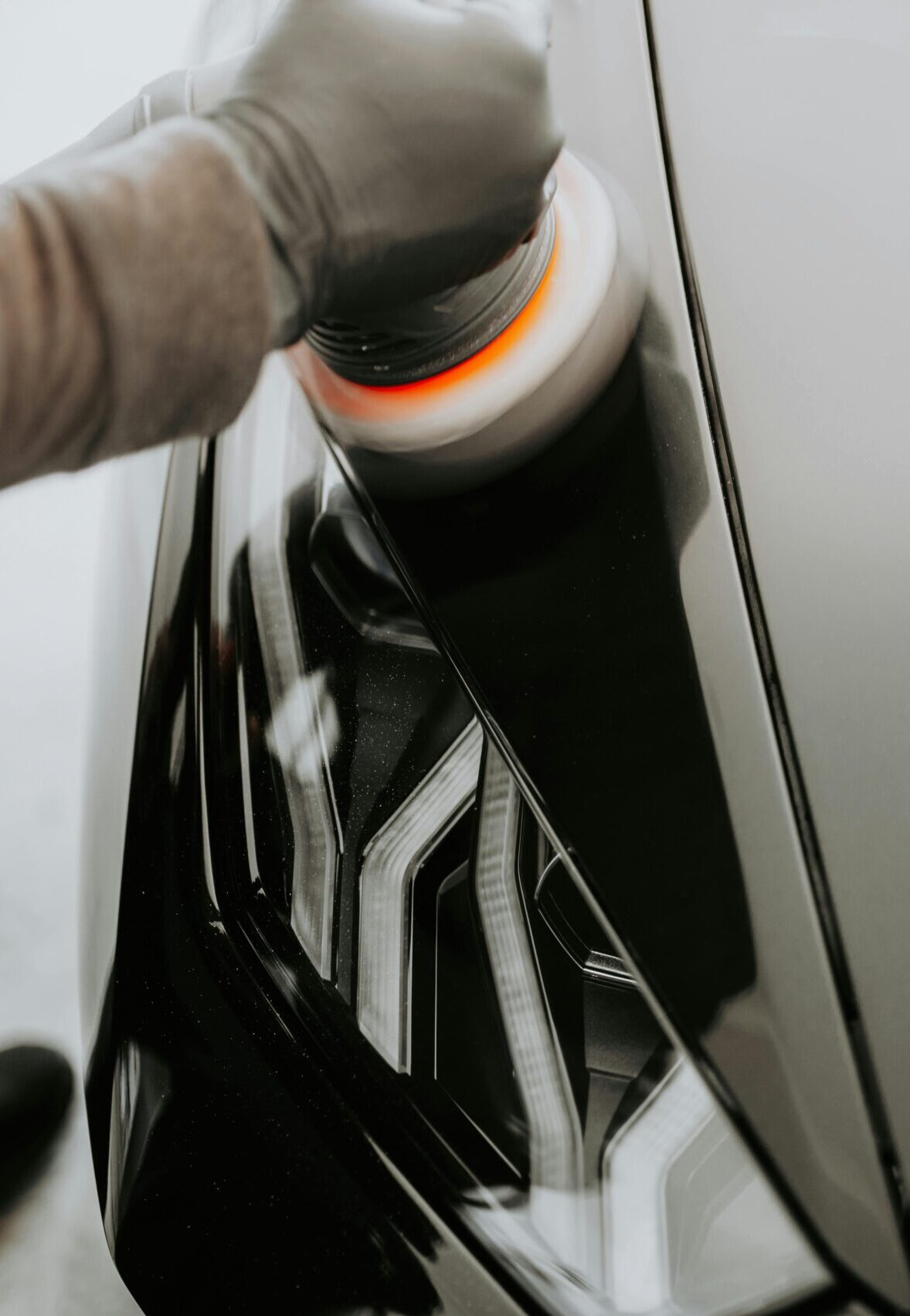 Close-up view of a person polishing a black car using a buffing machine.