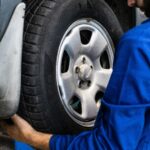 A mechanic in blue uniform closely examines a car wheel for repairs.